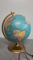 Front side view of the vintage globe showing Americas and part of Europe and Africa with gold-tone metal stand and power cord.