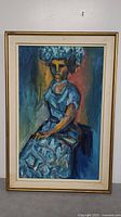 Full view of the framed oil painting showing the seated woman in blue dress and headdress, vibrant colors in background.