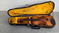 Violin shown in open case with yellow lining, black exterior case, violin positioned with bow compartment visible