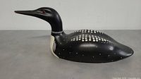 Front-side view of the black wooden loon carving showing red eyes and white painted spots on the back, smooth surface with some beak wear.