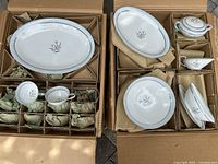 Two open boxes showing Noritake Bluebell china in original packaging, including platters, cups, saucers, sugar bowl, creamer and stacks of plates