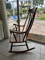 Side view of vintage wooden rocking chair showing curved armrest and spindle backrest.