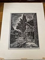 Full frontal photo of the black and white linocut print of a street scene with trees and buildings, including details of signed and titled areas below image.