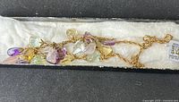 Top view of vintage necklace in box showing clusters of multicolored gemstone chips including citrine, amethyst, rose quartz, clear and green stones on gold-tone chain.