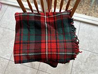 Folded wool blanket with red and green plaid pattern on a wooden chair.