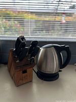 Photo showing the Hamilton Beach stainless steel electric kettle next to a Zwilling wooden knife block with several knives inserted.