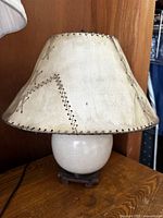 Full view of lamp showing rawhide stitched lampshade and rounded crackled ceramic base on carved wooden stand.