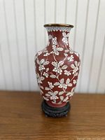 Front view of vintage Chinese cloisonne vase with red and white floral design on wooden stand.
