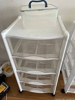 Rubbermaid 4-drawer storage unit with clear drawers and white plastic frame, showing the entire unit and the clear plastic box with blue handle placed on top.