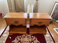 Two honey oak night tables with brass drawer handles placed side by side on a carpet. No visible scratches or damage except small divot in one drawer.