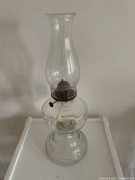 Full view of the antique clear glass and metal kerosene lamp showing overall shape and decorative base pattern.