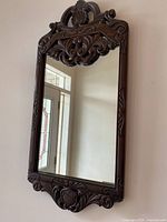 Full view of the antique dark brown wood framed mirror hung on a wall, showing rectangular shape and intricate carvings.