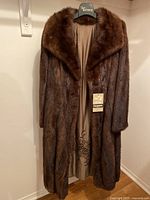 Full front view of long dark brown beaver fur coat hanging, showing collar and satin lining visible inside.