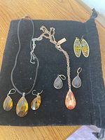 Seven jewelry pieces displayed on black fabric including two necklaces with amber colored glass pendants, matching earrings with amber glass drops, and multicolor beaded earrings.