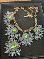 Gold-tone chain necklace laid flat in black box showing the blue and green dangling crystal pendants