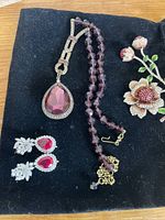 Photo showing the necklace with red faceted beads and large teardrop pendant, matching earrings with red teardrop stones, and the floral brooch with red and pink stones.
