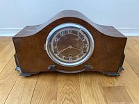Front view of wooden mantel clock with round brass bezel and clock face with Arabic numerals