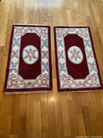 Two matching floral wool area rugs with burgundy background, floral border, and central oval floral medallion, placed side by side on hardwood floor.