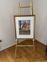 Full view of the framed print displayed on a gold stand, showing the artwork and setting.
