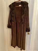 Front view of a large brown fuzzy bathrobe with a hood hanging on a door handle.
