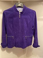 Front view of purple suede leather jacket hanging on hanger, showing front zipper and pockets with gold-tone zippers.