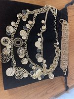 Full view of gold-tone necklace with various circular pendants and matching bracelet displayed on black cloth and wooden surface