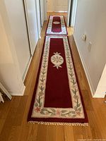 Two long burgundy hand-woven hallway runners on wooden floor, each about 2 feet wide and 8 feet long, with floral pattern borders and central floral medallions.