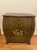 Front view of small brown wood chest of drawers showing three drawers with hand-painted floral and fruit design and round wooden knobs.