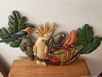 Full view of colorful handcrafted wooden tropical bird wall art showing multiple birds and green leaves.