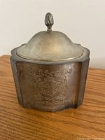 Front view of the zinc container showing engraved coat of arms and inscription.