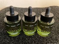 Three Korres Pure Greek Olive Early Harvest Vitality Shield Booster Oil bottles with droppers arranged side by side on a black surface.