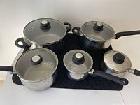 Photo showing all four pieces of cookware including a large pot with two handles and three saucepans with long handles, all stainless steel with glass lids.