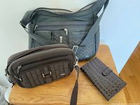 Two Lug brand bags and a brown alligator pattern wallet laid out on wooden table.