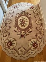 Oval ivory wool rug with floral and scroll design on wooden floor
