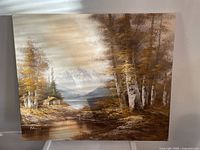 Full view of medium-sized oil on canvas landscape painting depicting autumn trees, cabin, mountains, and water body