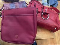 Three burgundy handbags and wallets arranged on table showing materials and logos.