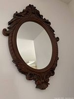 Front view of the ornate oval mirror showing the detailed brown frame with scroll and leaf pattern decoration.