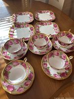 Overview of five tea cups with saucers and four square dessert plates arranged on table.