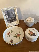 Overview photo showing porcelain pie plate, plastic fruit coaster container, 5x7 picture frame, and frosted glass vase with shells on wooden surface