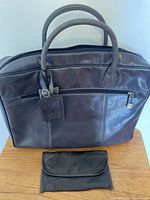Front view of dark navy leather briefcase and dark brown wallet on a wooden surface.