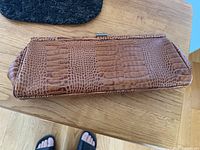 Top view of the tan crocodile embossed leather clutch showing texture pattern and metallic clasp closure.