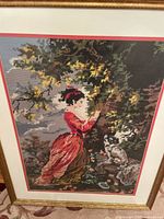 Full view of the framed Victorian needlepoint art showing the woman in a red dress beside a tree with a dog nearby.