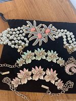 Full set of vintage necklace and earrings displayed on black cloth showing pearl necklace with floral rhinestone clasp, two floral enamel rhinestone chain necklaces, and pink crystal hoop earrings.