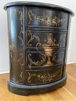 Front view of vintage black wood accent table with 4 drawers, decorated with hand-painted floral and gold scroll motifs.