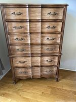 Front view of the vintage wooden dresser showing 7 drawers with curved fronts and decorative metal handles.