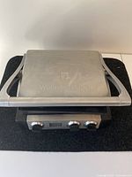 Full view of Wolfgang Puck electric griddle showing stainless steel top lid with logo and front control panel with three knobs and digital display.