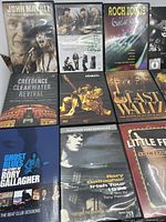 Photo shows a collection of 14 rock and blues guitarist DVDs with clear titles visible including John Mayall, Creedence Clearwater Revival, Rory Gallagher, The Last Waltz, Little Feat, and more.