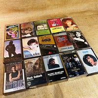 Photo showing all 15 cassette tapes arranged in three rows, featuring various artists such as Black Sabbath, Billy Ray Cyrus, Elvis Presley, The Tragically Hip, Martina McBride, Randy Travis, and Barry Manilow.