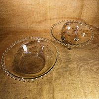 Two clear glass bowls with beaded edges on a textured fabric background.