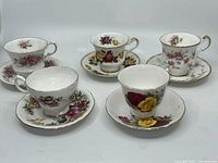 All five tea cups paired with their matching saucers, displaying varied floral patterns and gold trims